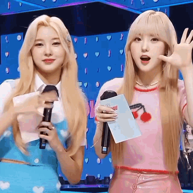 two blonde girls are standing next to each other on a stage holding microphones .