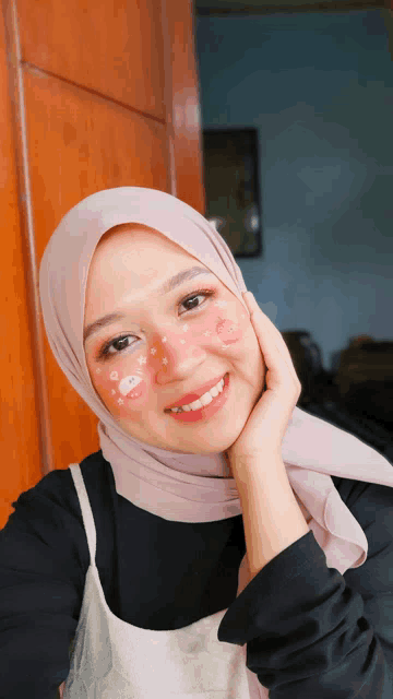 a woman wearing a pink hijab and a black shirt smiles for the camera