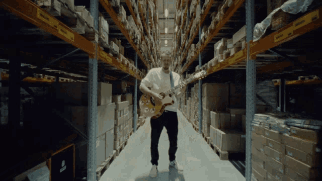 a man playing a guitar in a warehouse with a yellow sign on the shelves that says ' warehouse ' on it