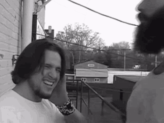 a man in a white shirt is smiling in a black and white photo with a building in the background