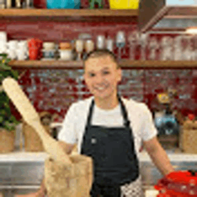 a man wearing an apron is standing in a kitchen holding a wooden spoon .