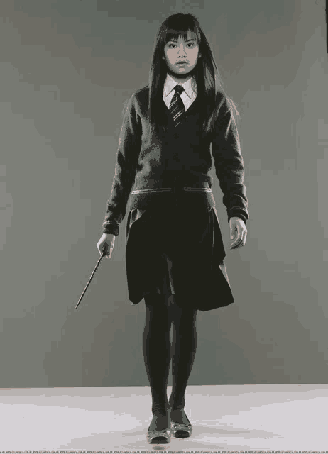 a girl in a school uniform holds a wand in her hand