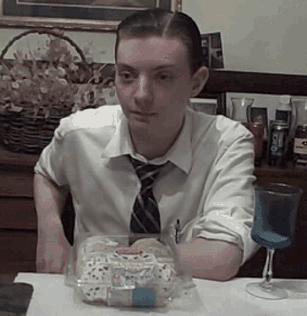 a man in a white shirt and tie sits at a table with a container of food in front of him