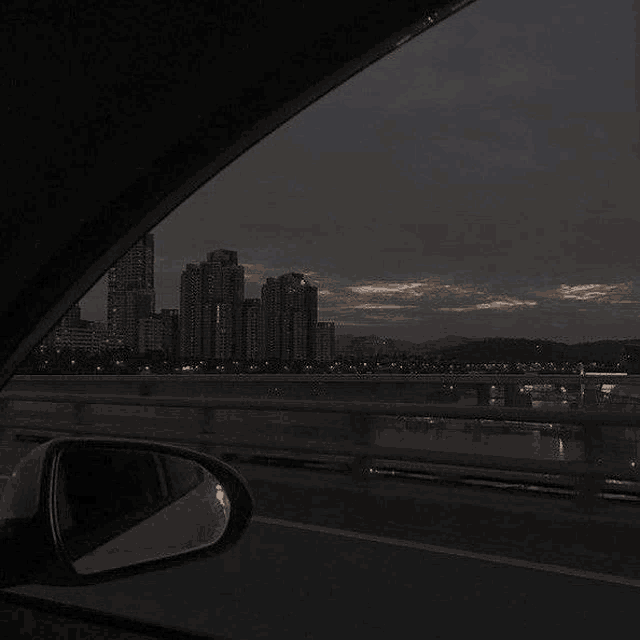 a car is driving down a highway at night with a view of a city skyline .