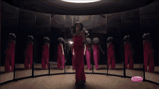 a woman in a red dress is dancing in front of a mirror with a pink button that says aotima on it