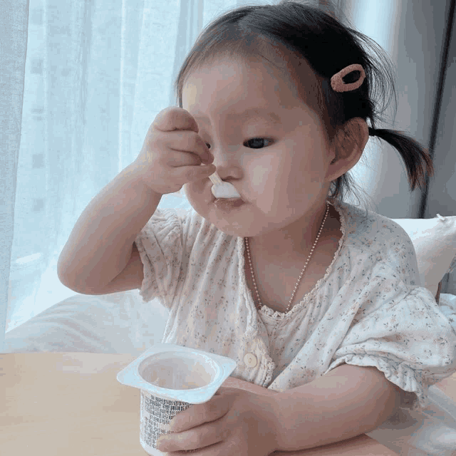 a little girl is eating yogurt from a container that says ' yogurt ' on it