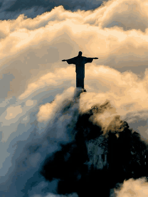 a statue of jesus is surrounded by clouds on top of a hill