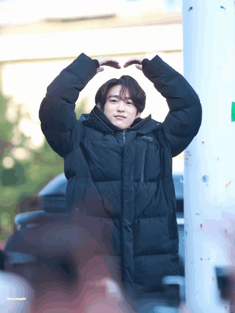 a young man in a black jacket making a heart shape with his hands