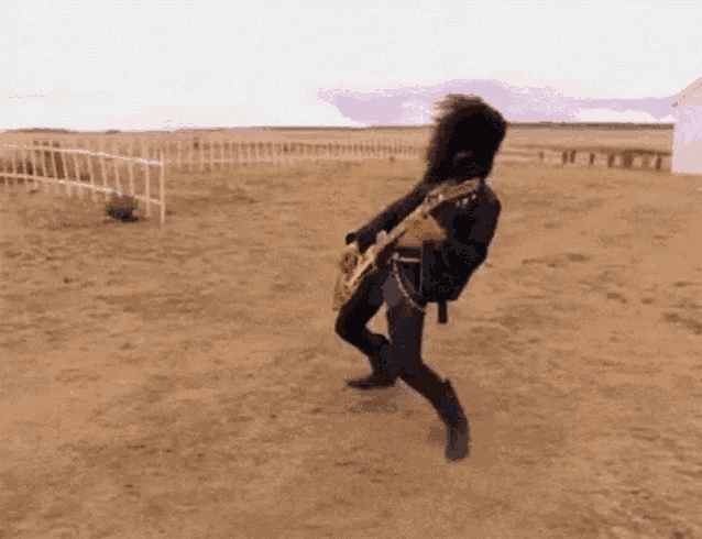 a man in a leather jacket is playing a guitar in the desert .