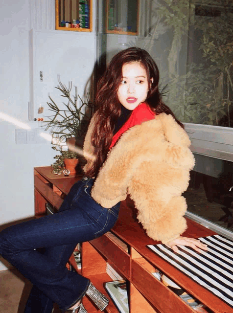 a woman wearing a fur coat sits on a shelf