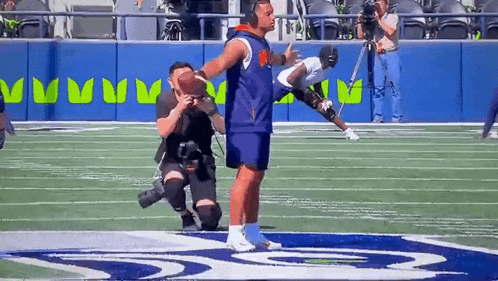 a man is holding a football on a field while a cameraman takes a picture .