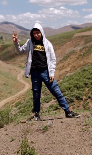 a person wearing a nike shirt is standing on a dirt road giving the peace sign