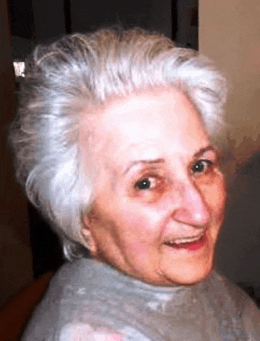 an elderly woman with gray hair and a grey turtleneck smiles for the camera