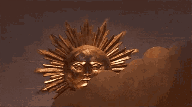 a gold sun with a face on it is hanging on the wall .