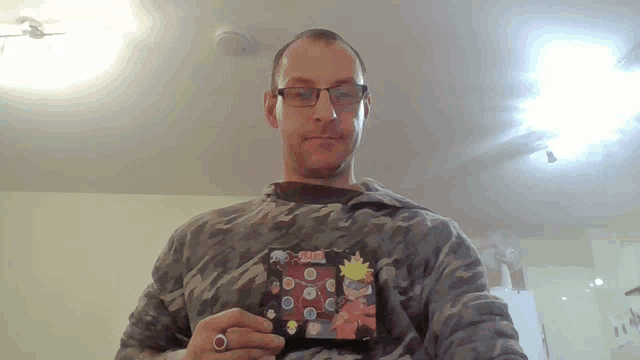 a man wearing glasses and a camouflage shirt is holding a naruto sticker