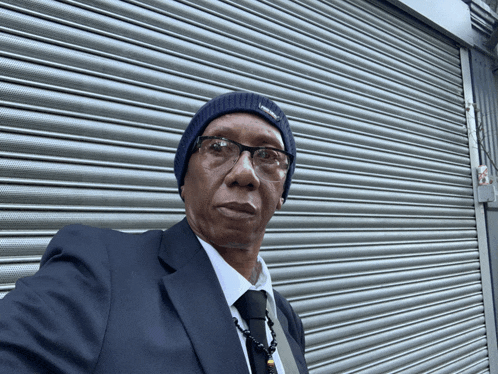 a man wearing a suit and tie is standing in front of a gray shutter