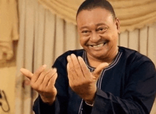 a man in a black shirt is smiling and clapping his hands in a living room .