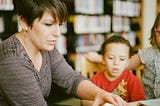 Teacher sitting at a table with a young boy, looking at a book