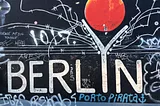 A black mural with the word “Berlin” spelt in white letters. The enlarged “Y” symbolized the Berlin Wall, which used to divide the city. On top, a red moon.