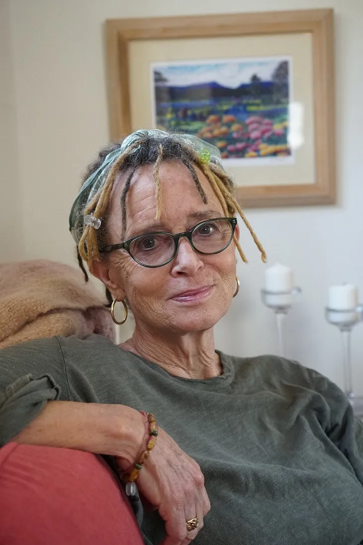 Photo of Anne Lamott looking with kind eyes toward the camera. Her hair is in dread locks, and she’s wearing cat-eye glasses. Love. Not Love. Compassion. Humor.