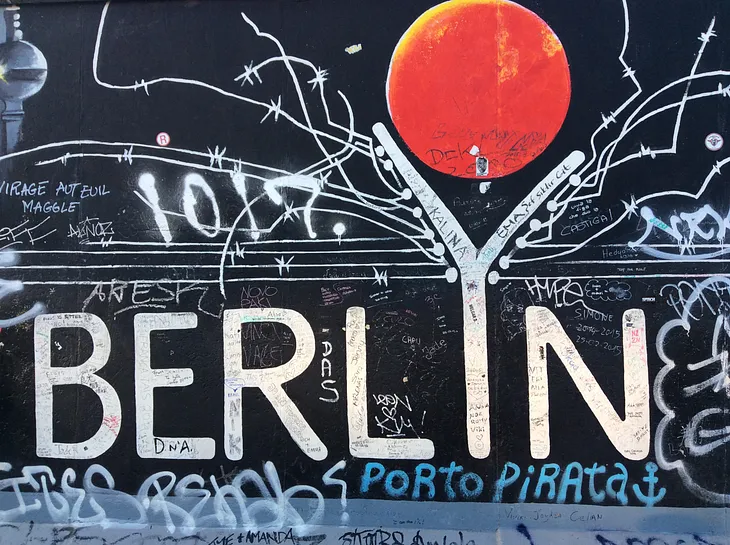 A black mural with the word “Berlin” spelt in white letters. The enlarged “Y” symbolized the Berlin Wall, which used to divide the city. On top, a red moon.