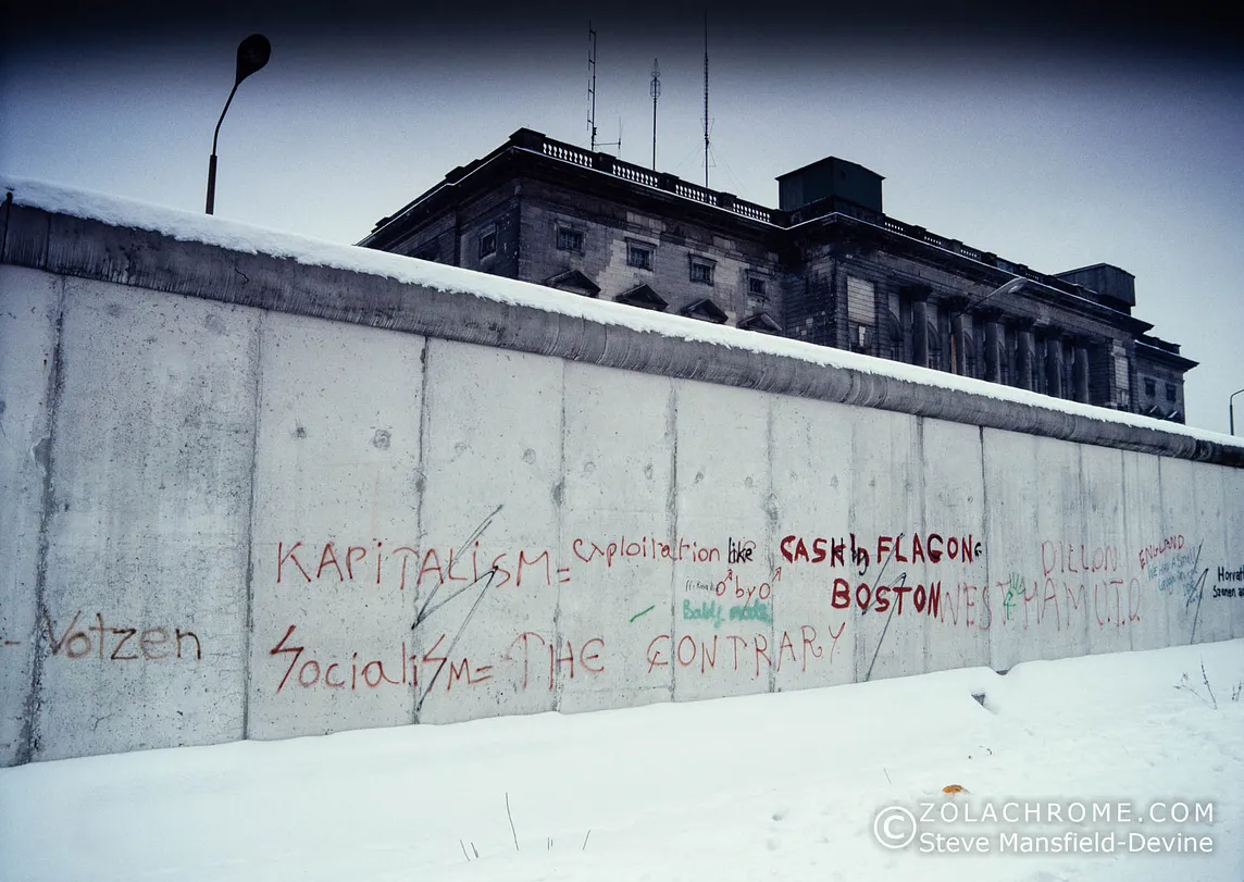 A sombre building in East Berlin appears behind the Berlin Wall which is covered in graffiti.