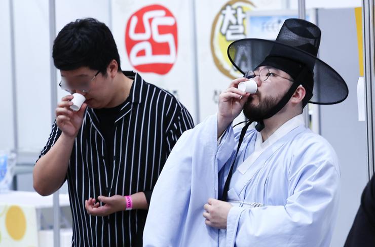 A visitor wearing traditional Korean costume tastes a sample of makgeolli, a Korean fermented rice alcoholic beverage, on the first day of the Korea Makgeolli Expo at aT Centerin southern Seoul, May 10. Newsis