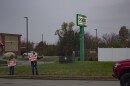 Two protesters — a woman holding a sign that reads "free baby supplies" and a man one that reads "adoption information available" — stand in front of a sign for the CHOICES Center for Reproductive Health in Carbondale on a grey, overcast day. They look small in the left corner of the frame, and there's a scrum of trees losing their leaves in the background.