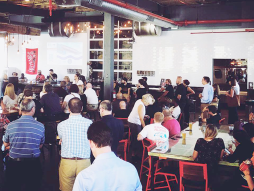 A crowd gathers at 4-Hands brewery around a stage. A panel of speakers delivers a presentation.