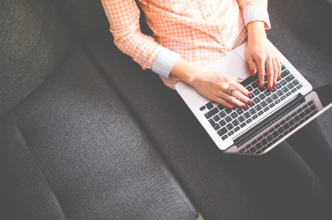 A women sits on a couch while typing on her laptop