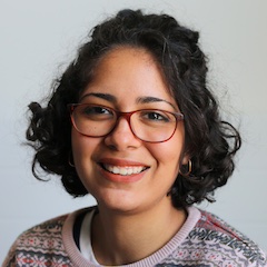 A smiling woman with dark hair and glasses wearing a jumper.