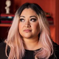 A woman with long multi-coloured hair dressed in black, looking to the side.