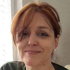 A smiling red-haired woman wearing earrings indoors.