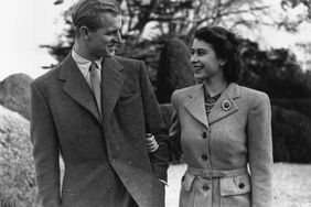 Prince Philip and Queen Elizabeth smile at one another while walking arm-in-arm outside.