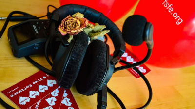 Podcast recorder and headphones with a rose and ballons in the background