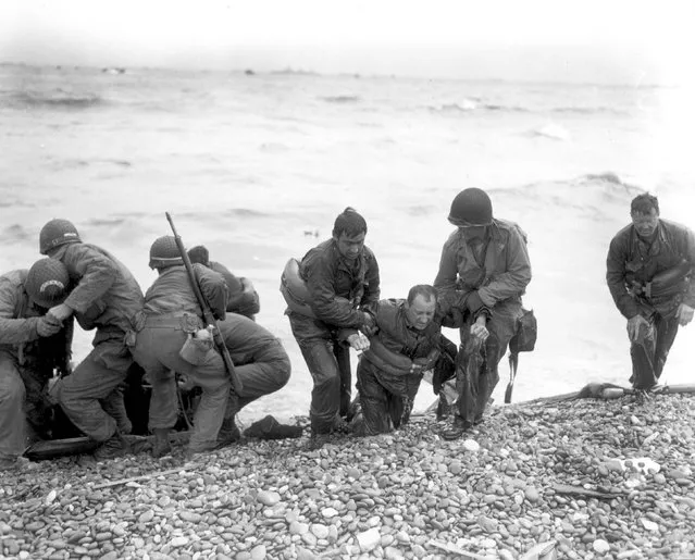 Members of an American landing party assist troops whose landing craft was sunk by enemy fire off Omaha beach, near Colleville sur Mer, France, June 6, 1944. REUTERS/Weintraub/US National Archives