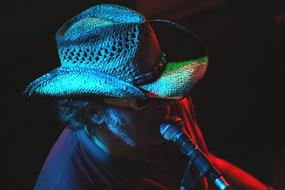 Singer in the hat, near the microphone, in colorful lights, at black background