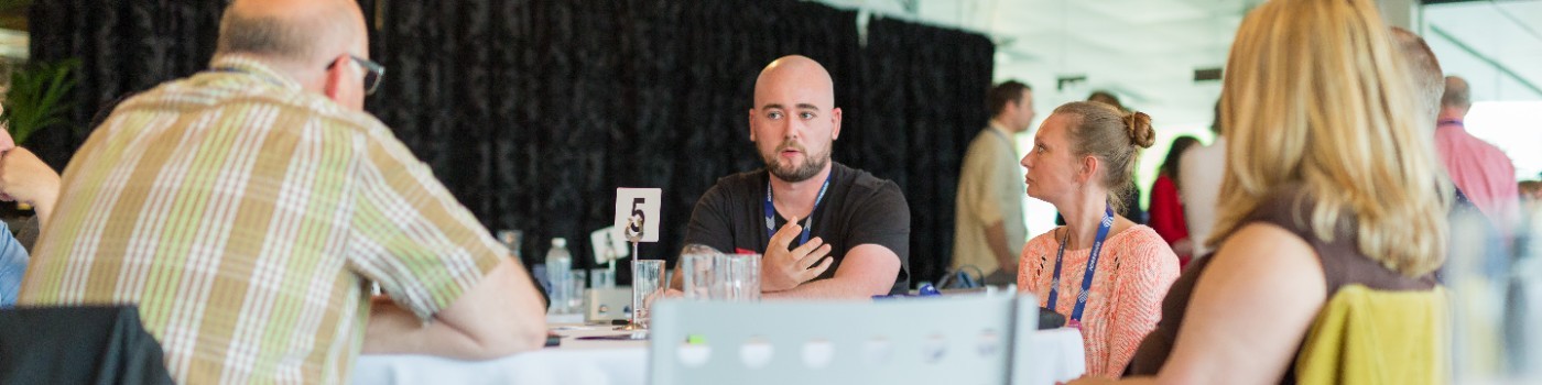 Shaun speaking to a group of people around a table at a conference