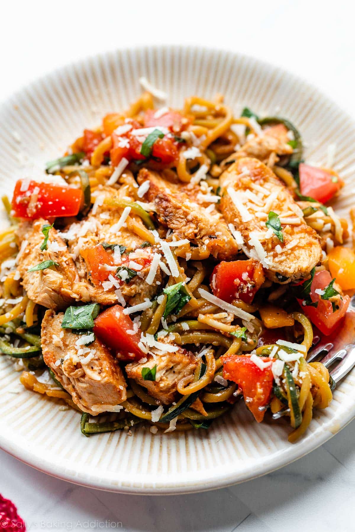 bruschetta chicken and zucchini noodles with parmesan cheese sprinkled on top on plate.