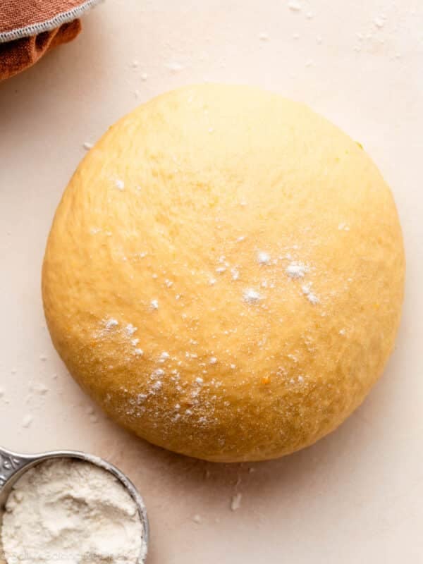 orange-colored dough with speckles of flour on top on peach backdrop.