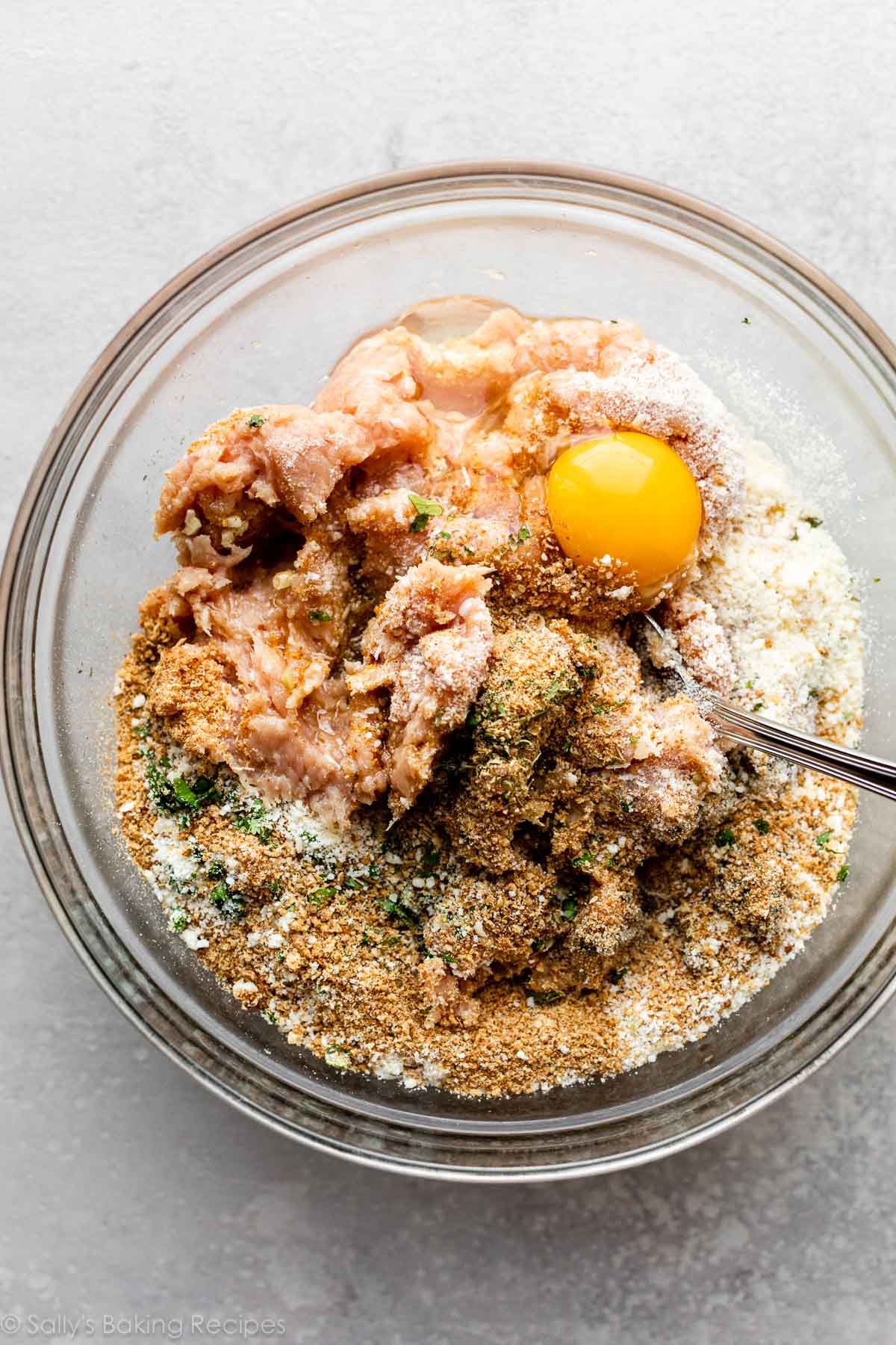 meatball mixture ingredients in glass bowl with spoon about to stir together.