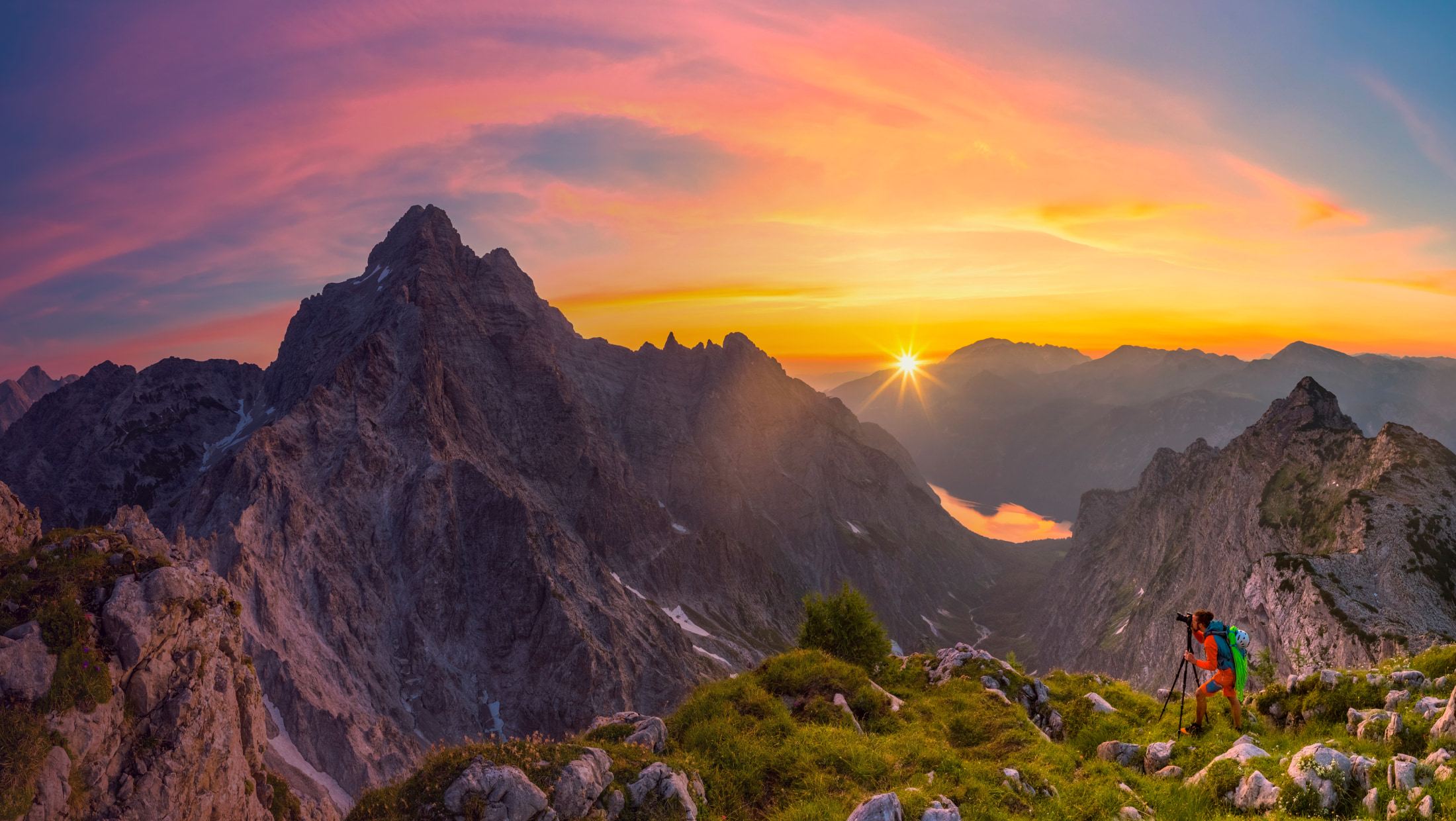 Mountain range scene during sunset, climber taking a photo in the lower right side.