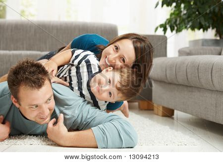 Happy family playing at home, lying heaped on floor in living room.