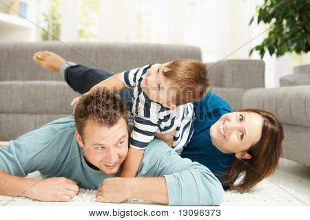 Happy family playing at home, lying heaped on floor in living room.