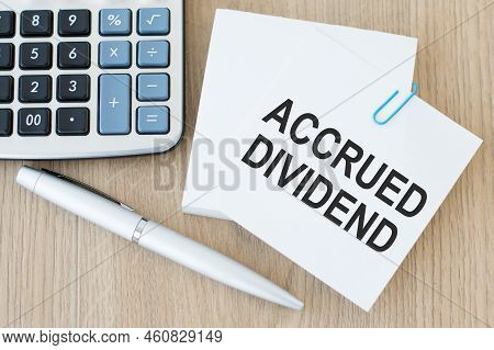 Accrued Dividend Inscription On A White Card On A Wooden Background Next To A Pen And Calculator