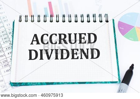 Accrued Dividend On A Sheet Of Notepad On The Table Against The Background Of Reports And Charts, Th