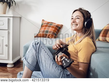 Woman playing ukulele at home. Domestic lifestyle. Woman relaxing at home. Hipster lifestyle. Beautiful woman at home. Lifestyle. Concept of easy living lifestyle. Happy people in at home. Relaxed people. Young people. Home decor. Playing music lifestyle.