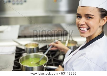 Young cheerful chef stirring sauce in professional kitchen