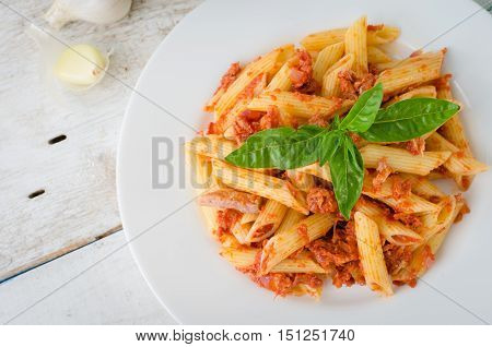 Italian Wholemeal Pasta Penne with Tuna and Basil. Fresh pasta with tuna and tomato sauce on white wooden background. Baked penne pasta with tuna fish and tomato sauce. Italian food concept. Top view.