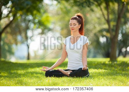 Yoga outdoor. Happy woman doing yoga exercises, meditate in the park. Yoga meditation in nature. Concept of healthy lifestyle and relaxation. Pretty woman practicing yoga on the grass